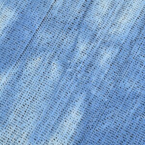 Pu&ograve; includere: Primo piano di un tessuto blu con un motivo intrecciato. Il tessuto ha una superficie leggermente ruvida e un colore blu chiaro.