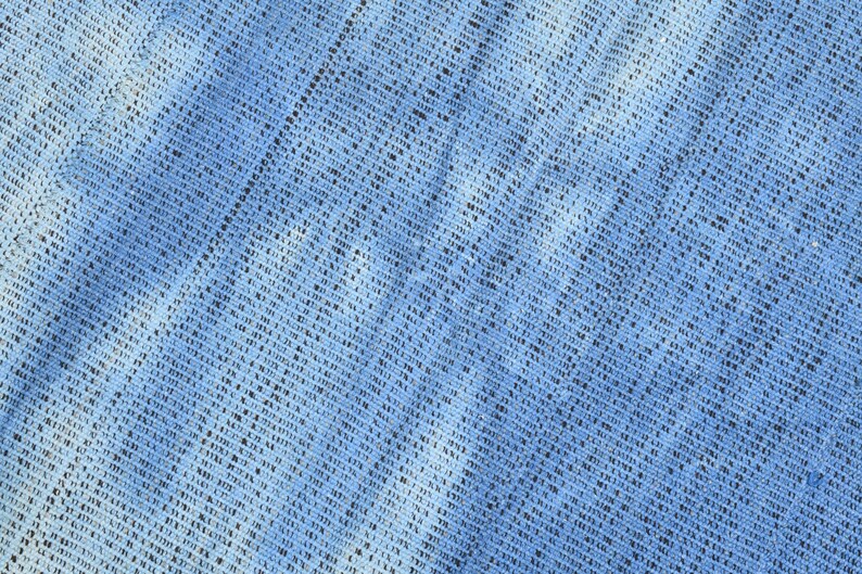 Pu&ograve; includere: Primo piano di un tessuto blu con un motivo intrecciato. Il tessuto ha una superficie leggermente ruvida e un colore blu chiaro.