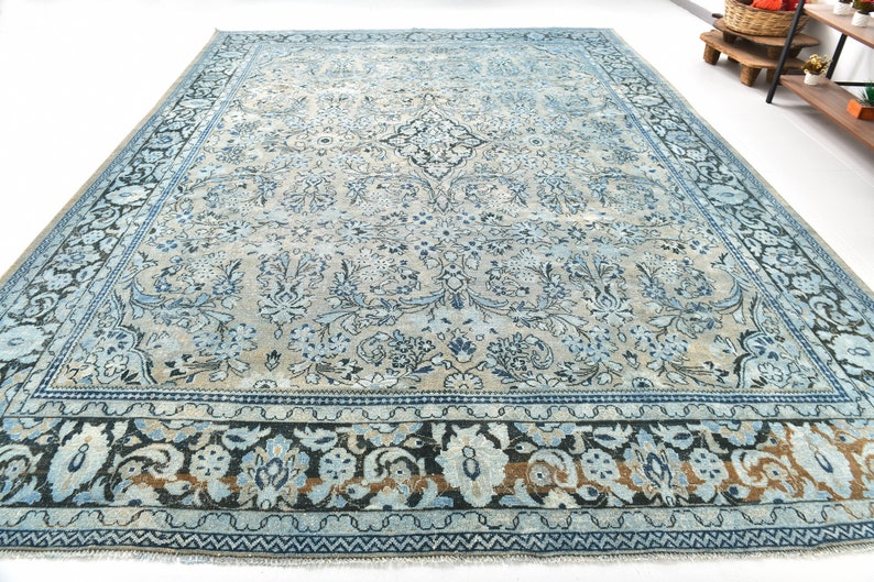May include: A vintage blue and cream rug with a floral pattern and a dark blue border. The rug has a worn and faded look, giving it a rustic and antique feel.