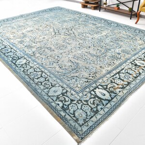 May include: A vintage blue and white rug with a floral pattern and a black border. The rug has a distressed look and is made of wool.