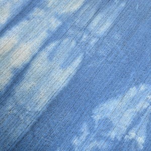 Pu&ograve; includere: Un primo piano di un tessuto blu con un motivo tie-dye bianco. Il tessuto ha un aspetto testurizzato e intrecciato.