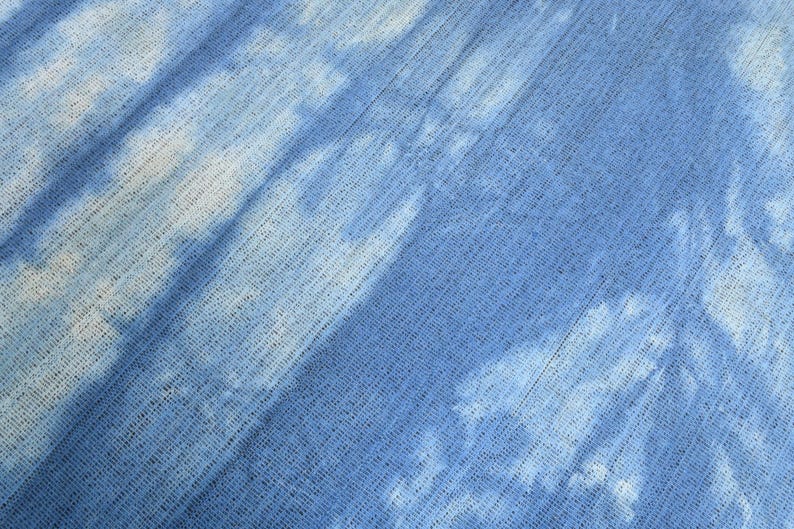 Pu&ograve; includere: Un primo piano di un tessuto blu con un motivo tie-dye bianco. Il tessuto ha un aspetto testurizzato e intrecciato.