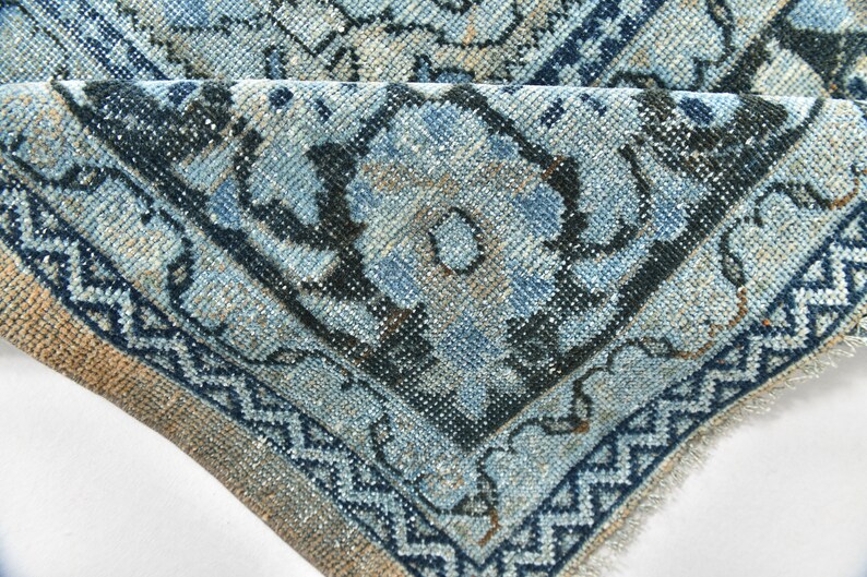 May include: Close-up of a blue and beige patterned rug with a fringed edge. The rug has a floral design with intricate details.