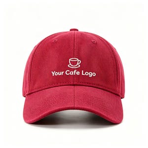 Pode incluir: Um boné de beisebol vermelho escuro com um gráfico bordado em branco de uma chávena de café num pires, posicionado sobre o texto branco Your Cafe Logo. O boné tem uma copa estruturada, uma aba curva e costuras visíveis nos painéis.