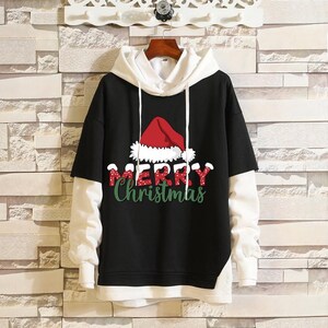 Könnte beinhalten: Schwarz-weißer Kapuzenpullover mit einem roten und weißen Weihnachtsmann-Hut-Motiv und dem Text "Merry Christmas".