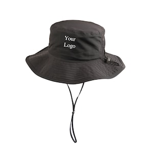 Puede incluir: Sombrero negro de cubo con un ala ancha y un cordón de ajuste negro. El sombrero tiene el texto "Your Logo" bordado en la parte delantera.