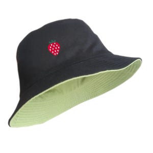 May include: Black reversible bucket hat with a light green interior. The exterior features an embroidered strawberry design. The hat is made of a soft fabric and has a wide brim. A stylish accessory for sun protection.
