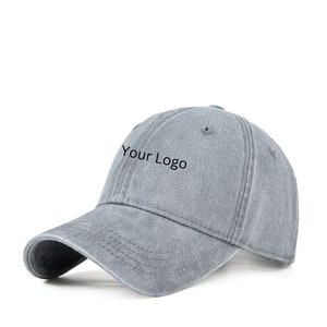 Peut inclure: Une casquette de baseball en coton gris avec un logo brodé noir qui dit "Your Logo".