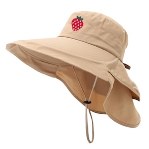 May include: A tan sun hat with a wide brim and a neck flap. The hat features a red and green embroidered strawberry on the front. It has an adjustable chin strap for a secure fit. The hat is designed for sun protection.