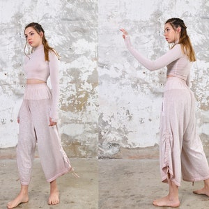 May include: A two-piece outfit in a light pink color. The top is a long-sleeved, high-neck crop top. The pants are loose-fitting and have a drawstring at the waist.
