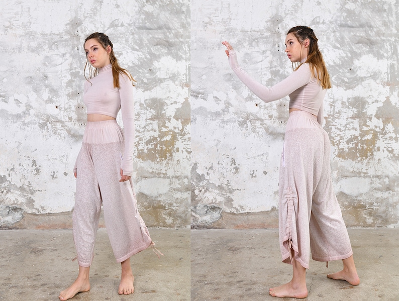 May include: A two-piece outfit in a light pink color. The top is a long-sleeved, high-neck crop top. The pants are loose-fitting and have a drawstring at the waist.