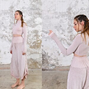 May include: A two-piece outfit in a pale pink color. The top is a long-sleeved, high-neck crop top. The pants are wide-legged and have a loose fit.