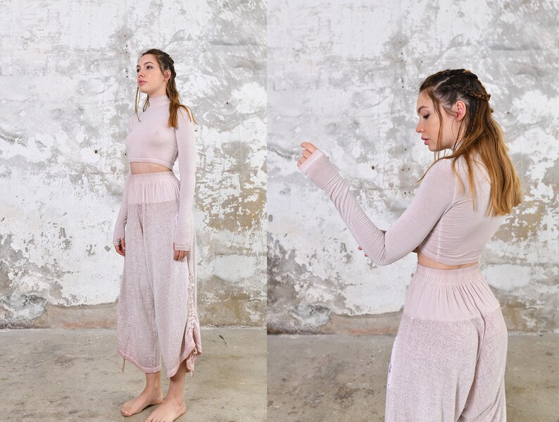 May include: A two-piece outfit in a pale pink color. The top is a long-sleeved, high-neck crop top. The pants are wide-legged and have a loose fit.