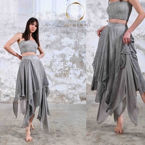 Puede incluir: Conjunto de dos piezas gris plateado, compuesto por un top corto y una falda asimétrica. La falda tiene paneles superpuestos y fluidos, creando una silueta dinámica y elegante. Adecuado para danza o ocasiones especiales.