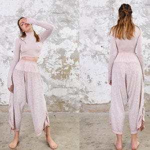 May include: A woman is wearing a light pink long-sleeved top and matching pants. The top has a high neck and the pants are loose fitting with a drawstring waist.