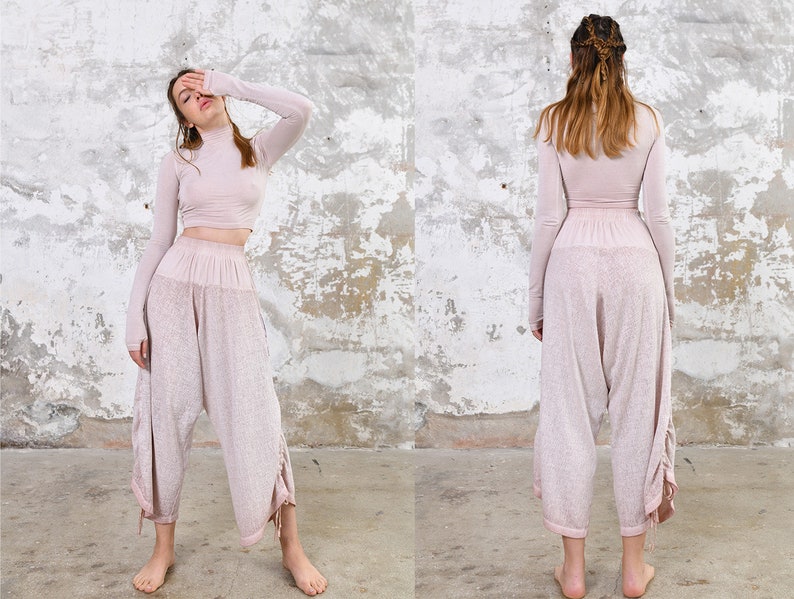 May include: A woman is wearing a light pink long-sleeved top and matching pants. The top has a high neck and the pants are loose fitting with a drawstring waist.
