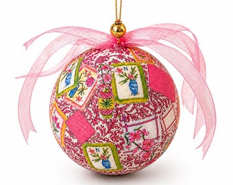 May include: A spherical ornament featuring a pink and white damask pattern background overlaid with rectangular illustrations of blue vases containing pink flowers, accented by a sheer pink ribbon and a gold hanging loop at the top.