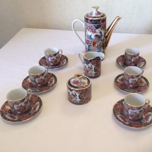Könnte beinhalten: Ein komplettes Vintage-Porzellan-Kaffeeservice mit einer hohen Kaffeekanne mit goldenem Ausguss, einem Sahnekännchen, einer Zuckerdose und sechs Tassen mit Untertassen. Das Set hat ein rotes, blaues und goldenes Blumen- und Pfauen-Design.