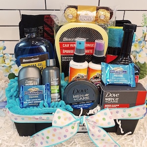 May include: A gift basket filled with men's grooming products, car care items, and chocolates. Includes car wash sponge, spray bottles, Dove Men+Care products, and Ghirardelli chocolate squares. The basket is decorated with a polka dot ribbon.
