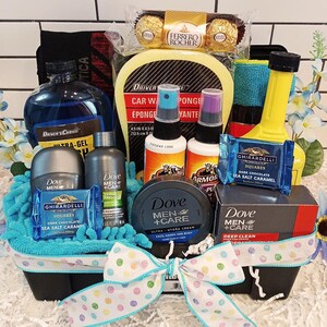 May include: A gift basket filled with car care products, Dove Men+Care toiletries, and Ghirardelli chocolate squares. The basket is decorated with a blue and white ribbon and a blue and white polka dot bow. The basket is filled with a variety of items, including car wash soap, a sponge, a car wash mitt, a bottle of Armor All, a bottle of Dove Men+Care body wash, a tube of Dove Men+Care face and body cream, and a bar of Dove Men+Care deep clean body wash.