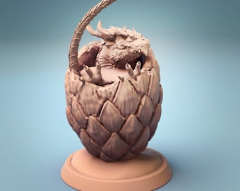 May include: A small, light brown dragon sculpture emerging from a cracked egg. The dragon has a long tail and is curled up inside the egg. The egg is on a round base.
