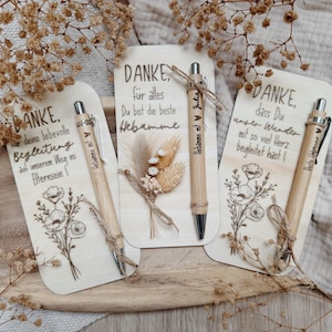 May include: Three wooden cards with engraved text and floral designs, each accompanied by a bamboo pen. The cards say "DANKE" in German, with additional text. Dried flowers and twine accents add a rustic touch to the presentation.