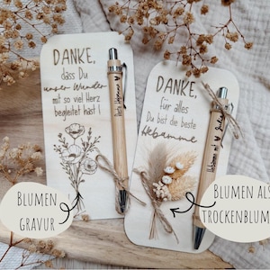 May include: Two wooden cards with engraved text and floral designs, accompanied by bamboo pens. One card features a poppy illustration, the other dried flowers. The pens are engraved with names.