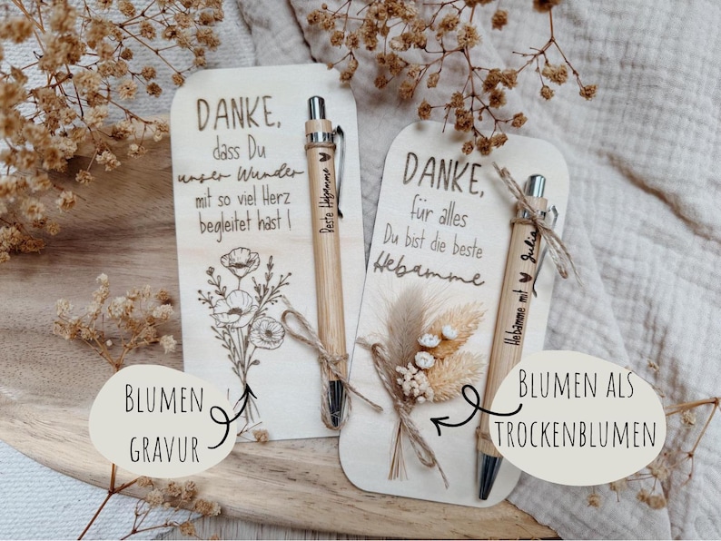 May include: Two wooden cards with engraved text and floral designs, accompanied by bamboo pens. One card features a poppy illustration, the other dried flowers. The pens are engraved with names.