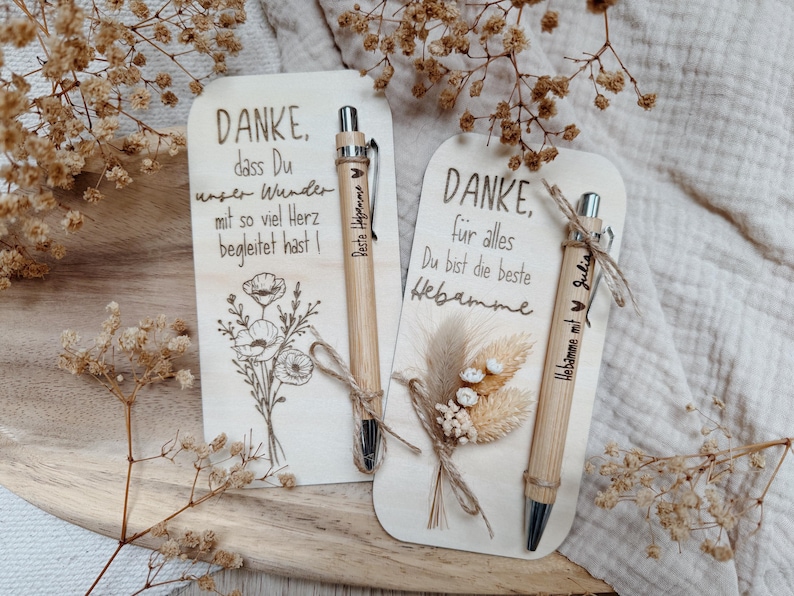 May include: Two wooden cards with German text and floral illustrations, accompanied by bamboo pens. One card says "DANKE" and the other says "DANKE, f&uuml;r alles". The pens have text and are tied with twine.