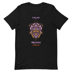 Puede incluir: Camiseta negra con un gráfico de robot morado y dorado. El gráfico está rodeado por un diseño geométrico. El texto "FOLLOW THE CODE - ETHICALLY" está impreso debajo del gráfico.