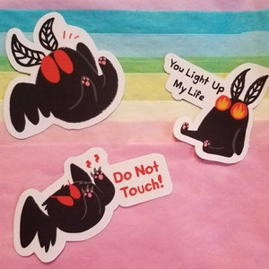 May include: Three black and red moth stickers with different expressions. The first sticker says "You Light Up My Life". The second sticker says "Do Not Touch!" The third sticker has no text.