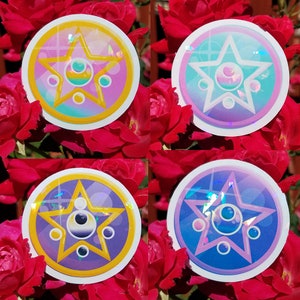 May include: Four round stickers with a holographic finish. Each sticker features a white star with a yellow outline and a circle with a black and white yin-yang symbol inside. The circles are surrounded by three smaller circles. The stickers are on a background of red roses.