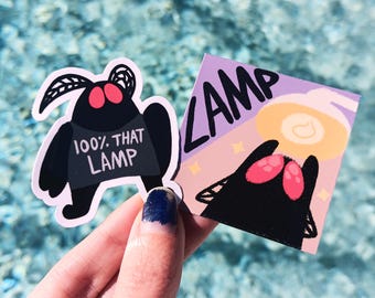 Könnte beinhalten: Zwei schwarze und rote Motten-Aufkleber. Ein Aufkleber hat den Text "100% THAT LAMP" darauf. Der andere Aufkleber hat den Text "LAMP" in großen Buchstaben.