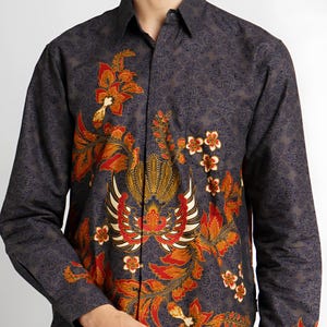 Op de afbeelding: Een overhemd met lange mouwen met een donkerblauwe achtergrond en een kleurrijk bloemenpatroon. Het patroon bevat rode, oranje, gele en witte bloemen en bladeren.