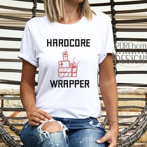 Könnte beinhalten: Weißes T-Shirt mit dem Text "HARDCORE WRAPPER" in Schwarz und einer roten Illustration von gestapelten Geschenken.