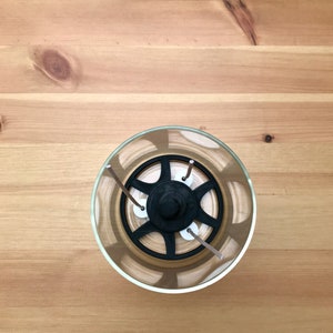 May include: A clear glass candle holder with a black, star-shaped insert and three wicks. The candle holder sits on a light brown wooden surface. The wicks are a light brown color.