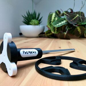 May include: A 3D-printed pizza cutter with a white and black handle and a silver blade. The handle has the text "PolMeks" printed on it. A black pizza cutter wheel is also present.