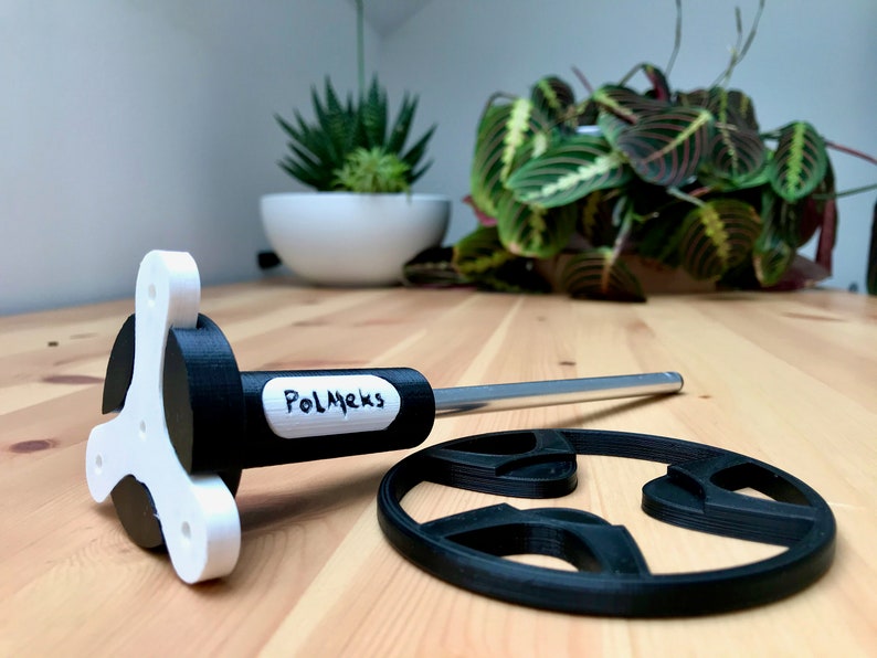 May include: A 3D-printed pizza cutter with a white and black handle and a silver blade. The handle has the text "PolMeks" printed on it. A black pizza cutter wheel is also present.