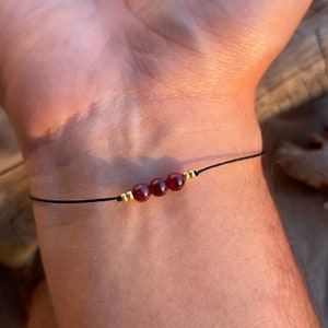 May include: A simple bracelet with three dark red beads and gold accents on a black cord.
