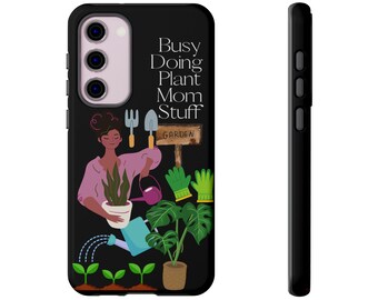Puede incluir: Carcasa de teléfono negra con una ilustración de dibujos animados de una persona haciendo jardinería. El texto "Busy Doing Plant Mom Stuff" está impreso en la carcasa. La carcasa tiene una carcasa de cámara negra con tres lentes.