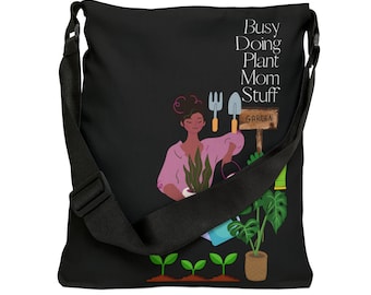 May include: Black canvas tote bag with a graphic of a person gardening. The text "Busy Doing Plant Mom Stuff" is printed on the bag. The graphic includes a watering can, gardening tools, and plants.
