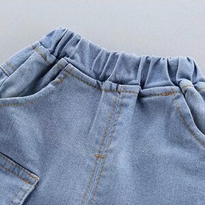 May include: Close-up of light blue denim shorts with an elastic waistband and pockets. The shorts have visible stitching in a contrasting tan color. The fabric appears to be a soft, lightweight denim.