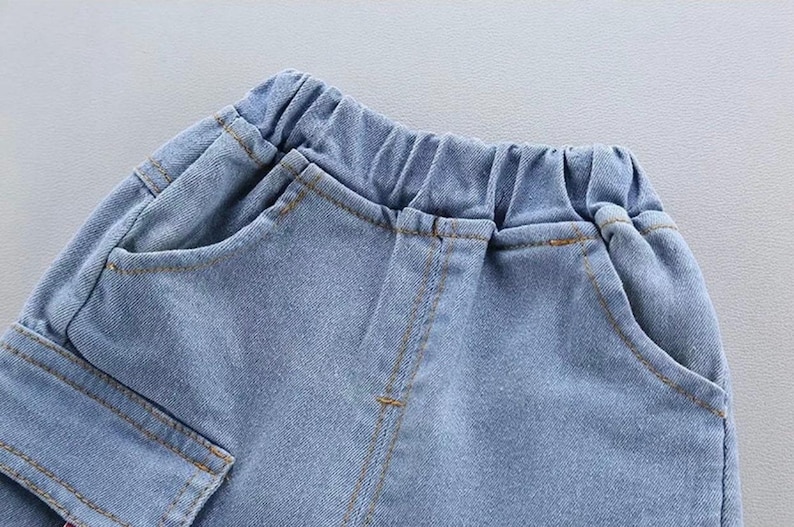 May include: Close-up of light blue denim shorts with an elastic waistband and pockets. The shorts have visible stitching in a contrasting tan color. The fabric appears to be a soft, lightweight denim.