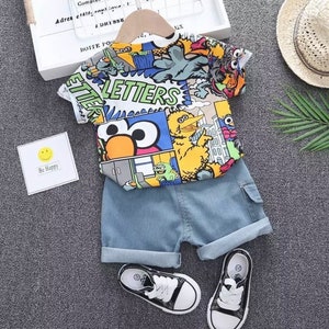 May include: A children's outfit featuring a colorful Sesame Street graphic t-shirt and denim shorts. The shirt has a vibrant print of characters and the word "LETTERS". Includes black and white sneakers.