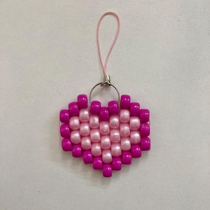 Puede incluir: Un llavero de cuentas en forma de corazón rosa y magenta con un anillo plateado y una cuerda rosa.