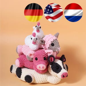May include: A collection of handmade crochet farm animals in shades of pink, white, and black. The stack includes a cow, pig, sheep, and two chickens. The animals are arranged on a light orange background.