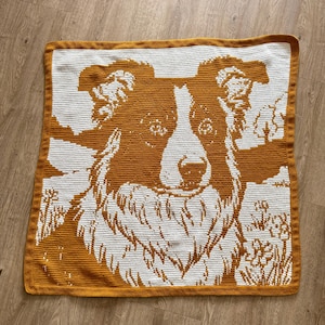 Peut inclure: Une couverture carrée au crochet avec une image détaillée du visage d'un chien. Le visage du chien est dans les tons de marron et de blanc, avec une bordure marron. La couverture est probablement faite à la main et convient à la décoration intérieure.