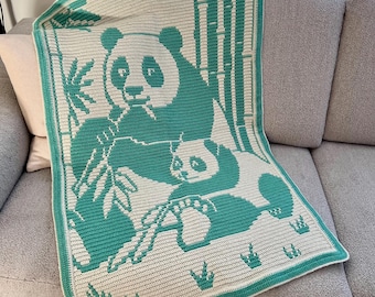 May include: A crocheted blanket in teal and white, depicting a panda bear and cub with bamboo. The blanket has a teal border. The design features a panda holding bamboo, with a smaller panda cub. The blanket is folded on a sofa.