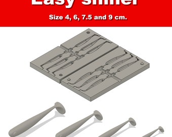 May include: A gray plastic fishing lure mold with the text "Easy shiner" and size measurements in centimeters. Four gray fishing lures of varying sizes are displayed below the mold. The sizes are 4, 6, 7.5, and 9 cm.