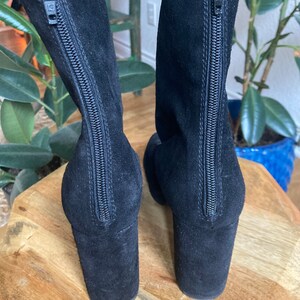 May include: A pair of black suede ankle boots with a zipper up the back. The boots have a block heel.